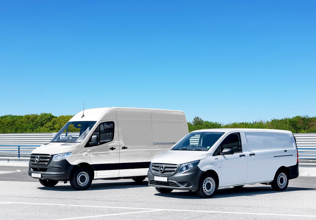 Two white delivery vans parked in a spacious parking lot under a clear blue sky.