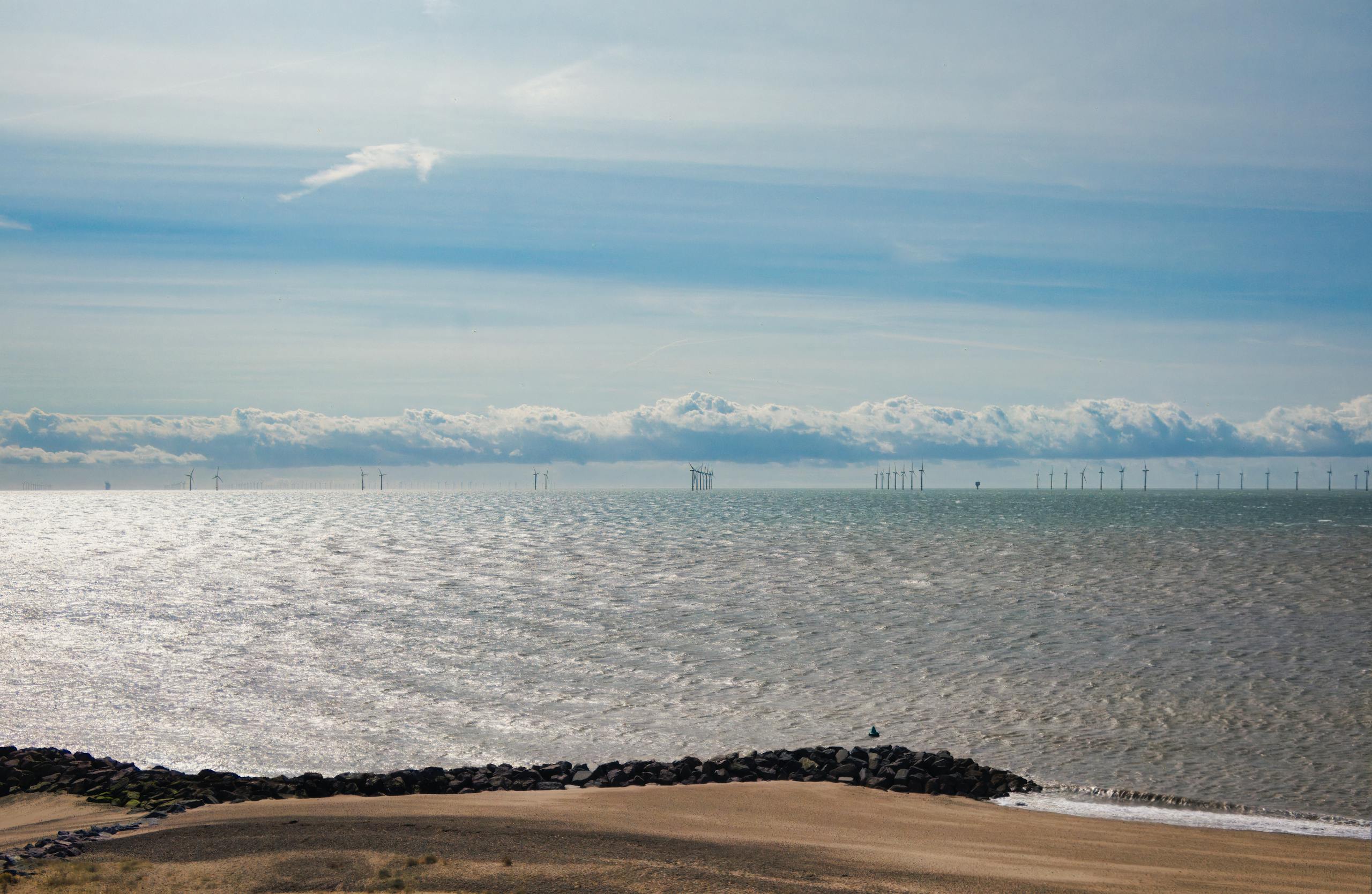 Scenic view of Clacton-on-Sea beach and wind turbines on a bright day.